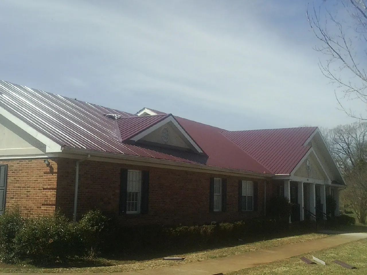 Red metal roof with gabled entries on a long brick building, from a Hail Damage Roof Repair job in Mansfield