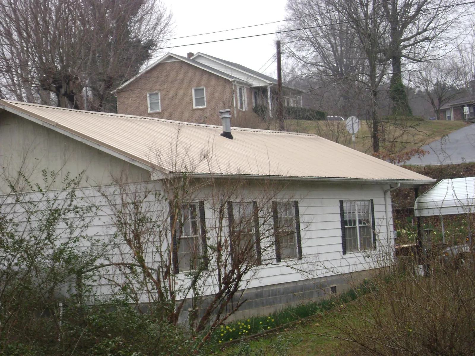 Tan metal roof on a white sided house set into a hillside — Commercial Roofing by Roofing Brothers in Mansfield
